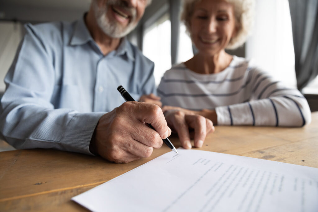 Close up focus on wrinkled male hand signing paper document.